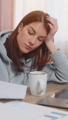 tired young woman freelancer using laptop computer at table with documents in living room at home