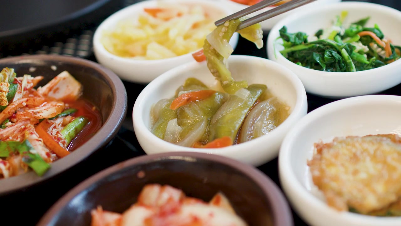 다양한 전통 한식 반찬의 클로즈업 샷, 젓가락으로 발효 채소를 집어 올리는 모습.