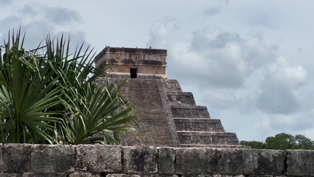 Handheld panning shot of El Castillo ancient Mayan pyramid rising above a wall at Chichen Itza in Yucatan, Mexico. 4K