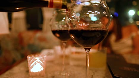 a wine bottle pours into glasses on a candlelit table, creating a warm, inviting atmosphere