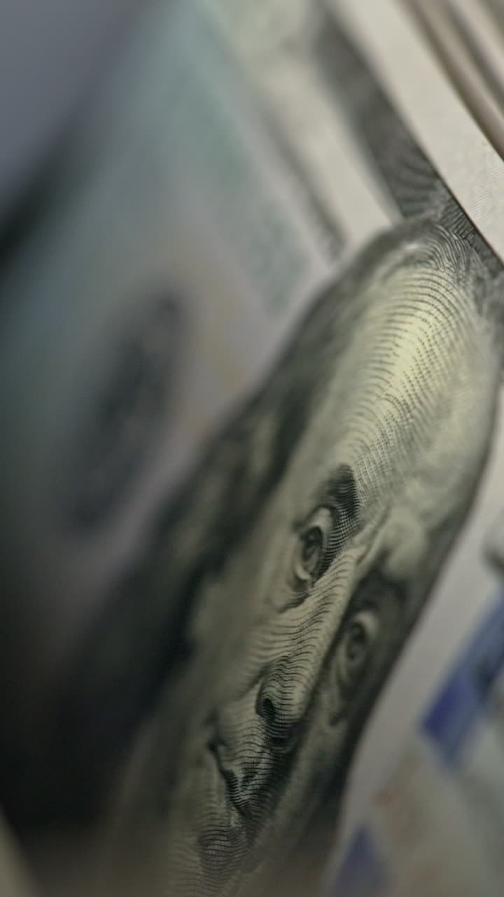 A number of hundred dollar bills with Benjamin Franklin portrait moving into money counting machine. Equipment for cash operations. Close up. Vertical video