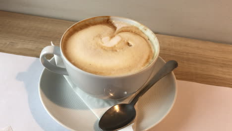 white coffee cup with heard latte art on milk foam standing on wooden board