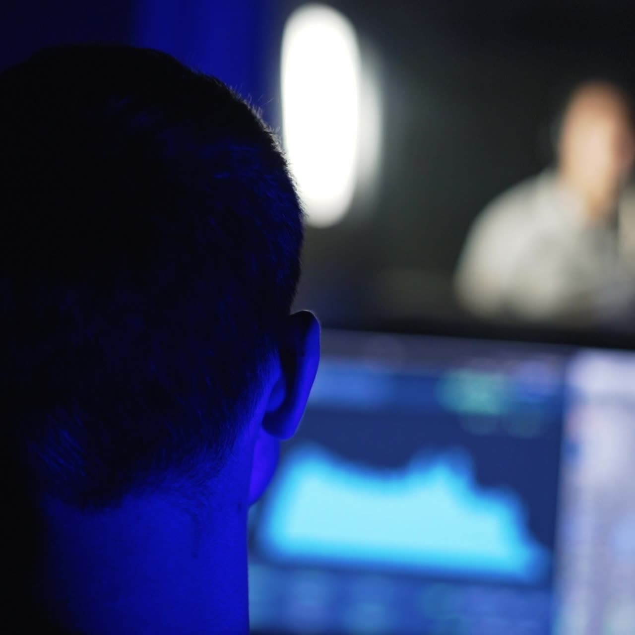 Rear view of a sound engineer's head working in front of computer screen in the professional studio. Duet performs at backdrop in a window in blur