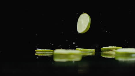 rings of green lime sliced fall on the glass with splashes of water in slow motion