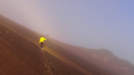 woman in yellow jacket climbs foggy volcanic ash slope on mountain