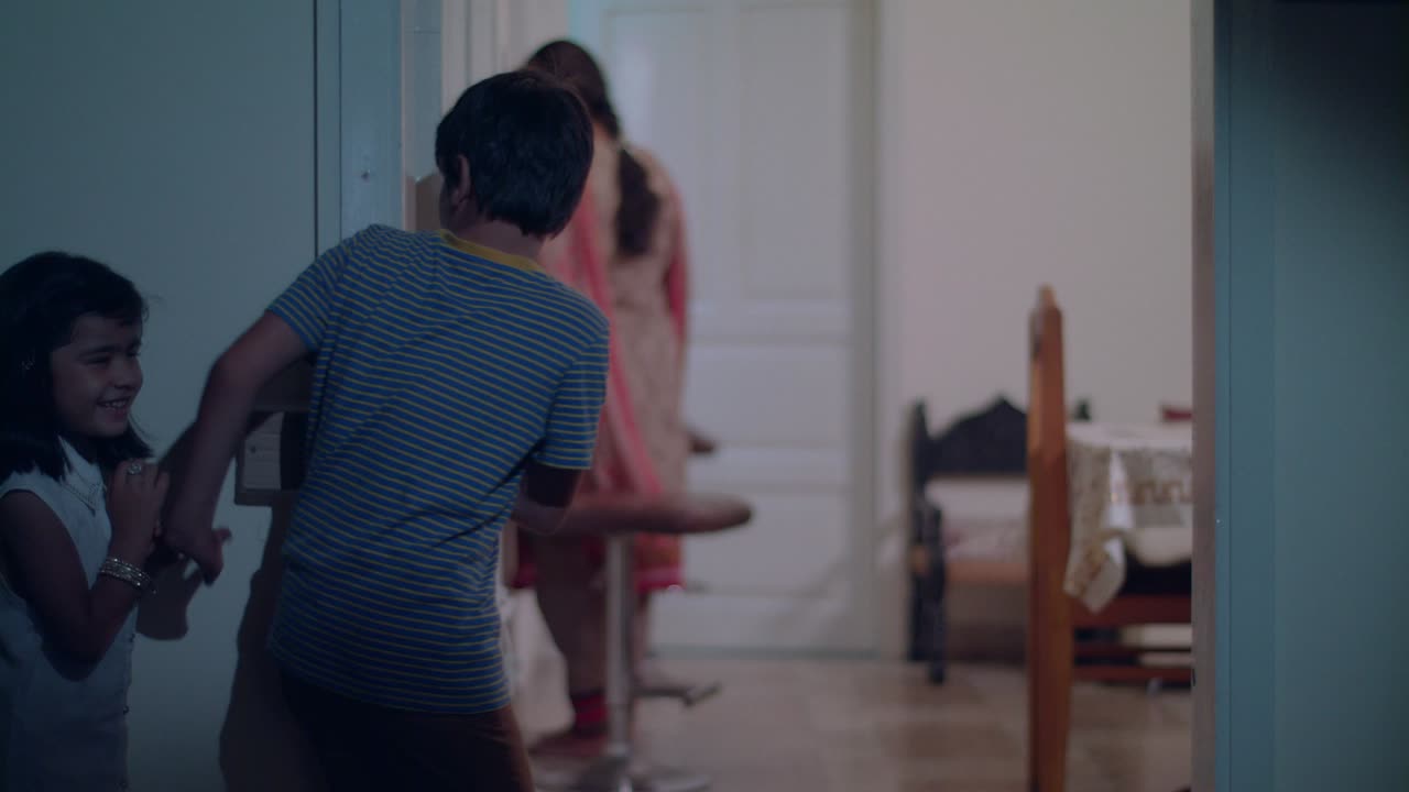 형제는 여동생에게 크로스오버를 조용히 그리고 비밀리에 신호를 보내고 어머니는 이드 준비를 위해 거실에서 일합니다.