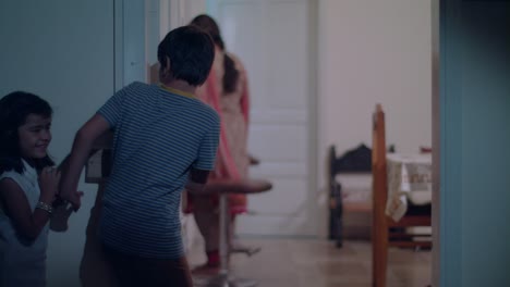 brother signals sister to crossover quietly and secretly as their mom works in the living room preparing for eid