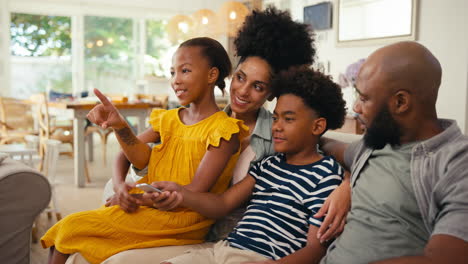 Familia-En-Casa-Sentada-En-El-Sofá-Juntos-Transmitiendo-Un-Programa-O-Una-Película-A-La-Televisión