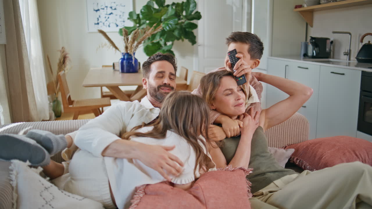 Happy family embracing sofa at home closeup. Funny kids hugging parents at couch