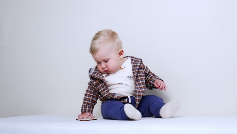 beautiful blond baby boy in checkered jacket sits on the floor. serious infant is playing with the wooden sign. vertical video.