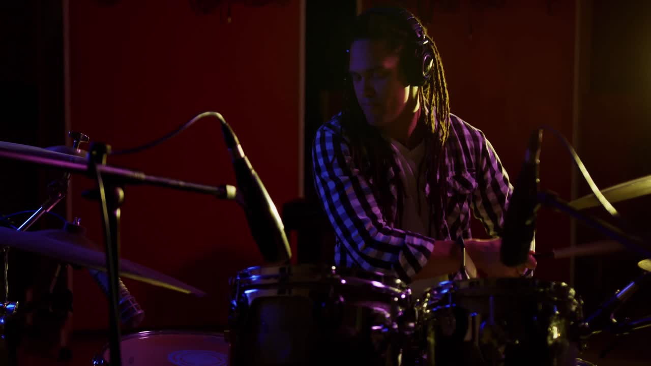 Mand med dreadlocks, der spiller trommer i et musikstudie.