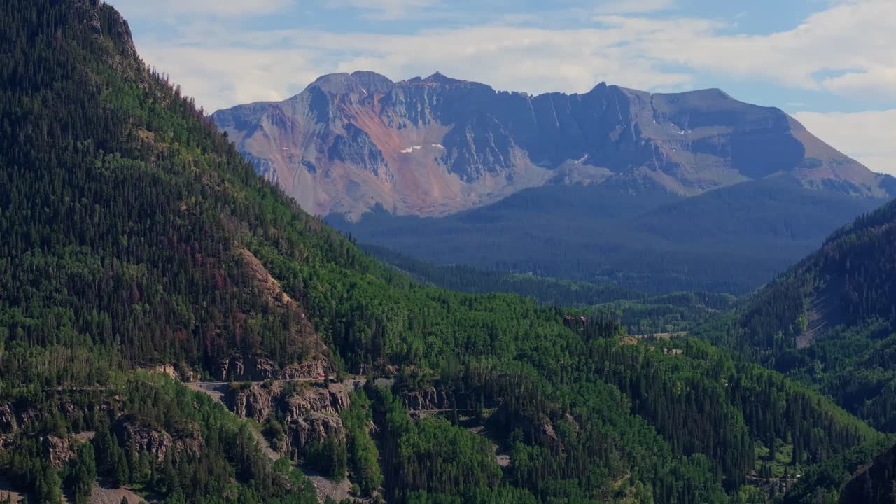 Valle di montagna con fitta foresta verde e cime a strati sotto un cielo estivo luminoso, Highway 145 Colorado USA