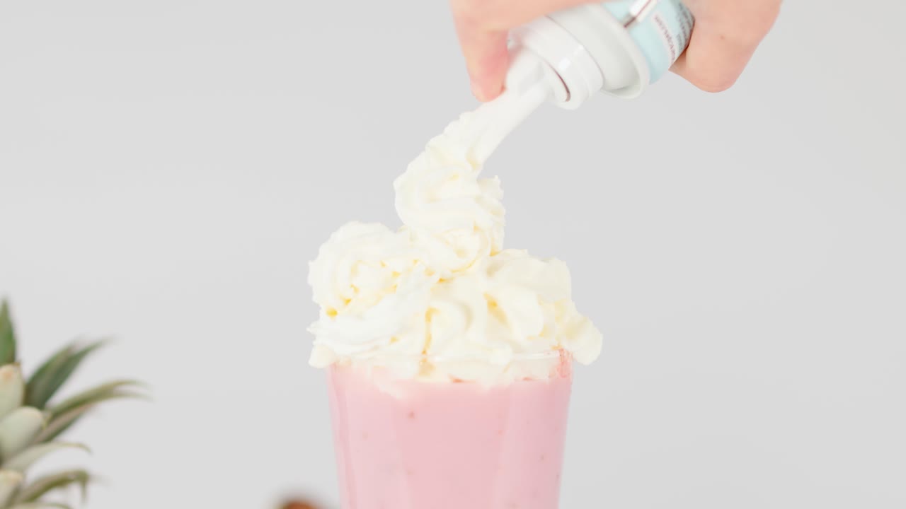Hånd sprøyter krem på rosa fruktsmoothie i glass, sterkt studiolys, statisk bilde