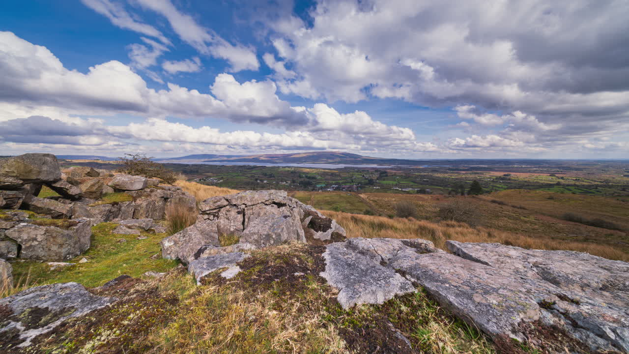 Panorama motion time lapse of rural landscape with foreground of rocks and grass on hillside and lake in the distance on a spring sunny cloudy day in Arigna mountains in county Leitrim in Ireland