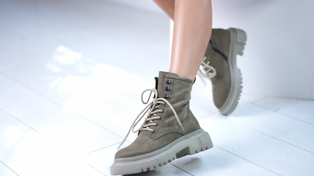 Demonstrating grey stylish modern boots with laces. Fashionable winter footwear with tractor soles on female hands. Close up. White backdrop.