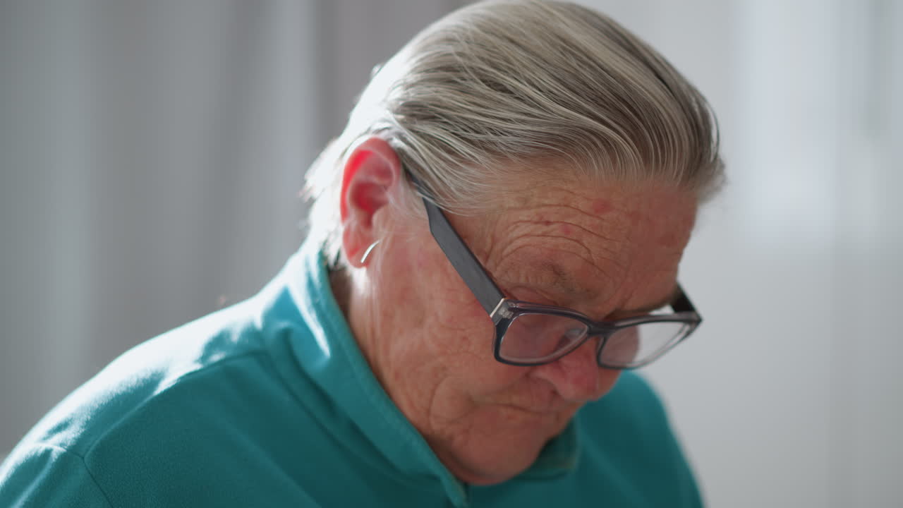 Close-up of elderly person adjusting glasses, looking thoughtful, with a focused expression. Soft lighting and indoor setting highlight effort in reading or examining something