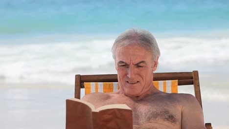 Älterer-Mann,-Der-Auf-Einem-Strandkorb-Sitzt-Und-Ein-Buch-Liest