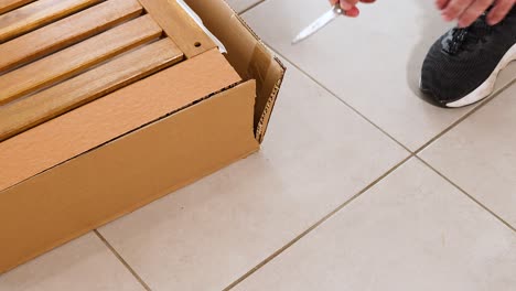 a person opens a cardboard box on a tiled floor, revealing wooden slats. bright lighting enhances visibility