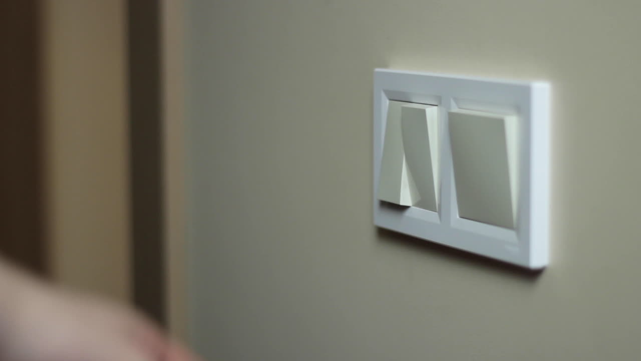 una mano caucásica enciende y apaga un interruptor de luz blanca, detalle de cerca