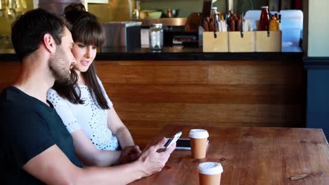 Couple-sitting-in-restaurant-looking-at-mobile-phone