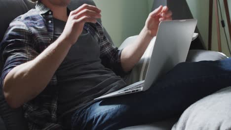 hombre caucásico feliz sentado en el sofá en la sala de estar usando una computadora portátil