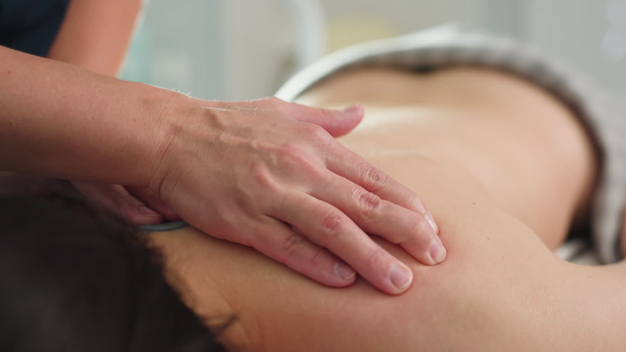Close up of body of spa guest being massaged by professional fingertips during session on massage bed under soft lighting in tranquil spa room creating soothing wellness atmosphere and calm