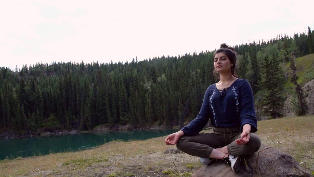 Indian woman meditates on rock at Miles Canyon, medium shot