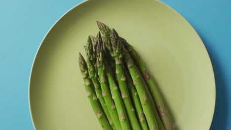 video of fresh asparagus on green plate over blue background