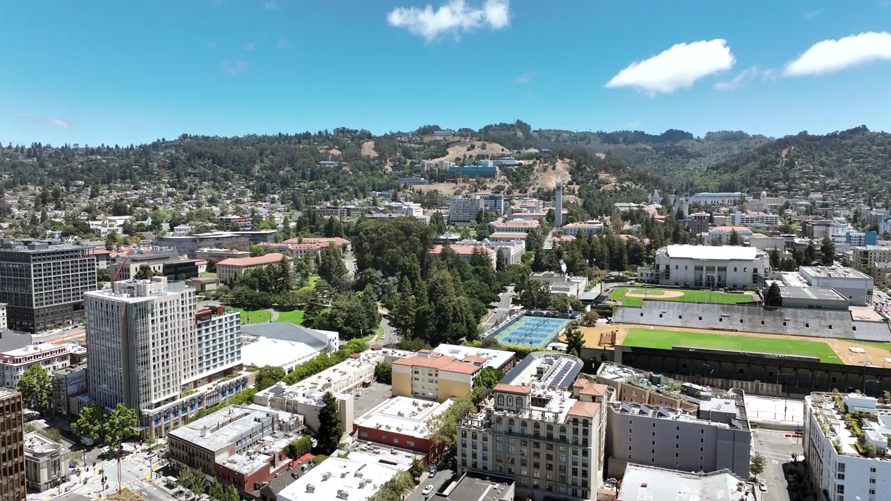 Filmato fluido in ascesa con drone su downtown Berkeley, California, che rivela edifici urbani, quartieri residenziali alberati, strade cittadine e le dolci colline di East Bay in lontananza