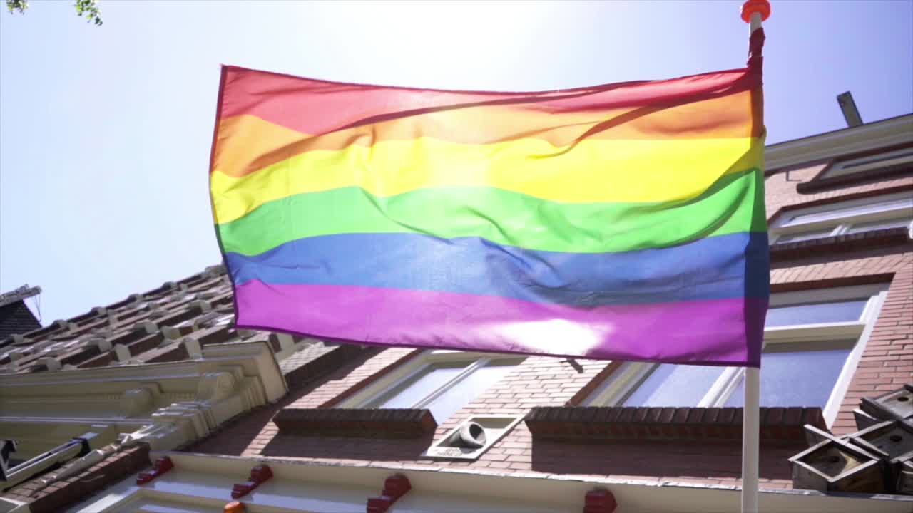 cámara lenta: una bandera del arco iris ondeando con las fachadas de las casas de amsterdam detrás de ella en un día soleado