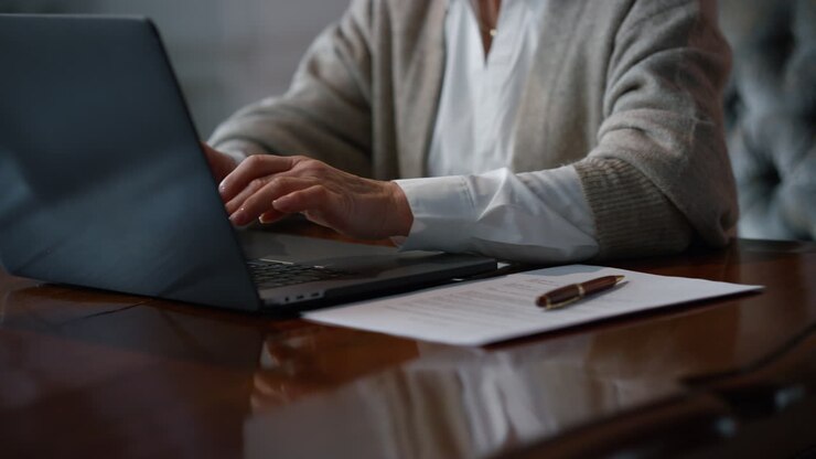 Mani di donna anziana che digitano su un laptop in un interno di lusso