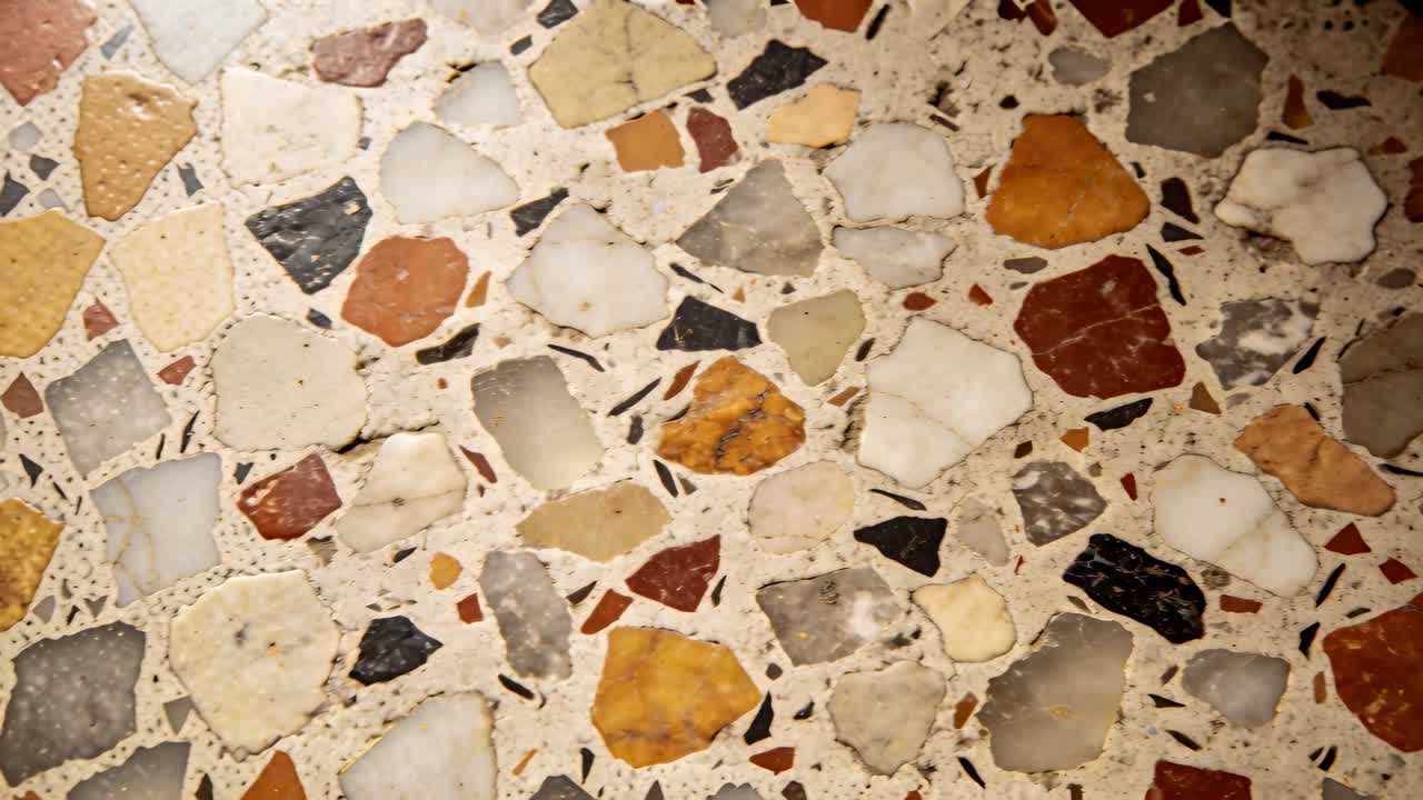 Telecamera che si muove ampiamente filmando un pavimento in terrazzo mentre la luce si sposta, mostrando scheggiature, avvallamenti e scintillii nella sala.