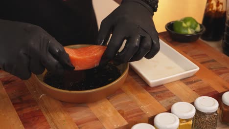 faceless chef wearing black gloves, marinating salmon fish fillet with citrus ponzu sauce prior to cooking, adding extra flavor and soften the texture of the fish