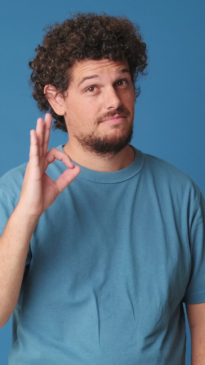 Uomo sorridente fa il gesto dell'OK su sfondo blu da studio