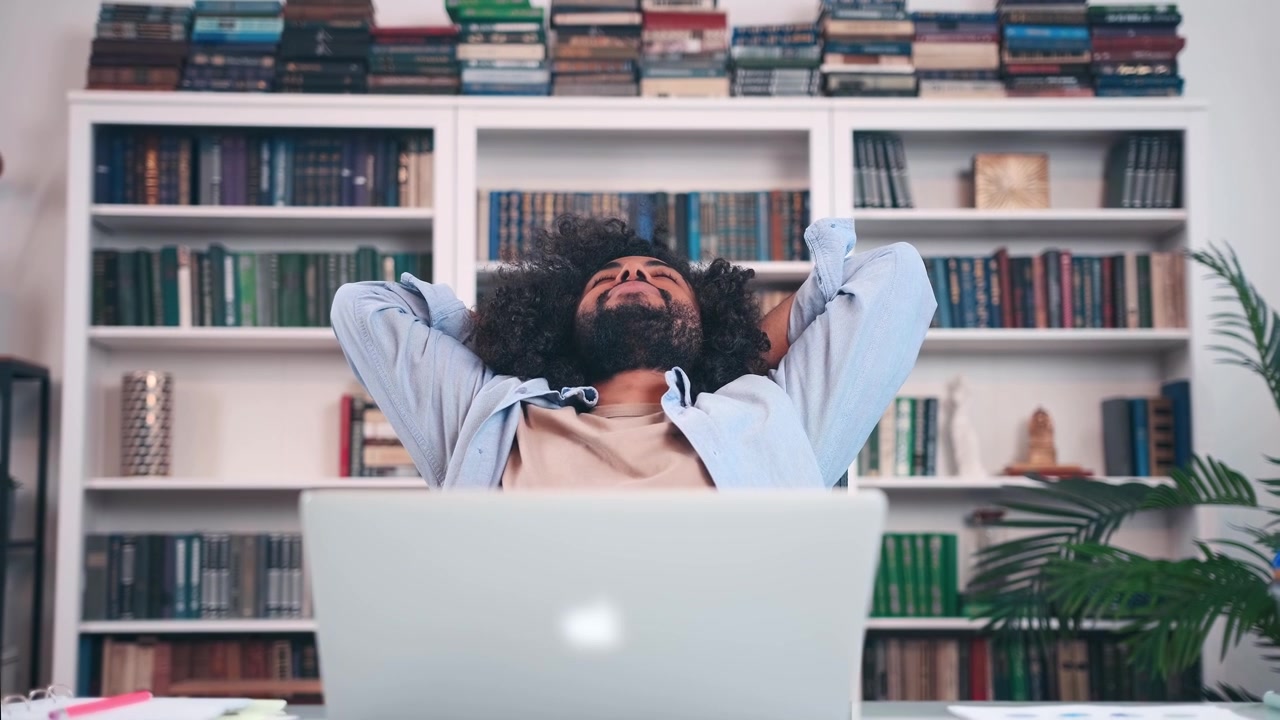 Relaxed Young Man Stretching at Desk in Home Office