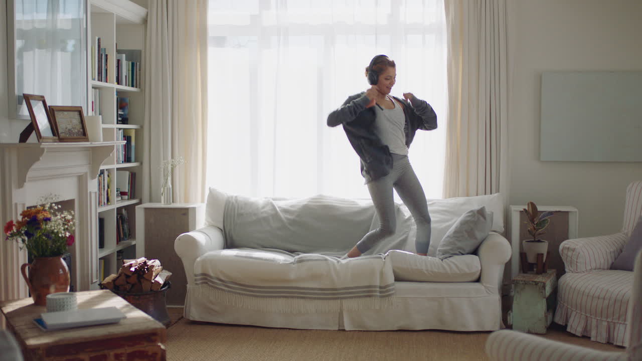 행복한 젊은 여성이 집에서 춤을 추고 즐겁게 음악을 듣고 헤드폰을 착용하고  ⁇ 키 댄스 동작으로 주말 축제를 즐기고 있습니다.