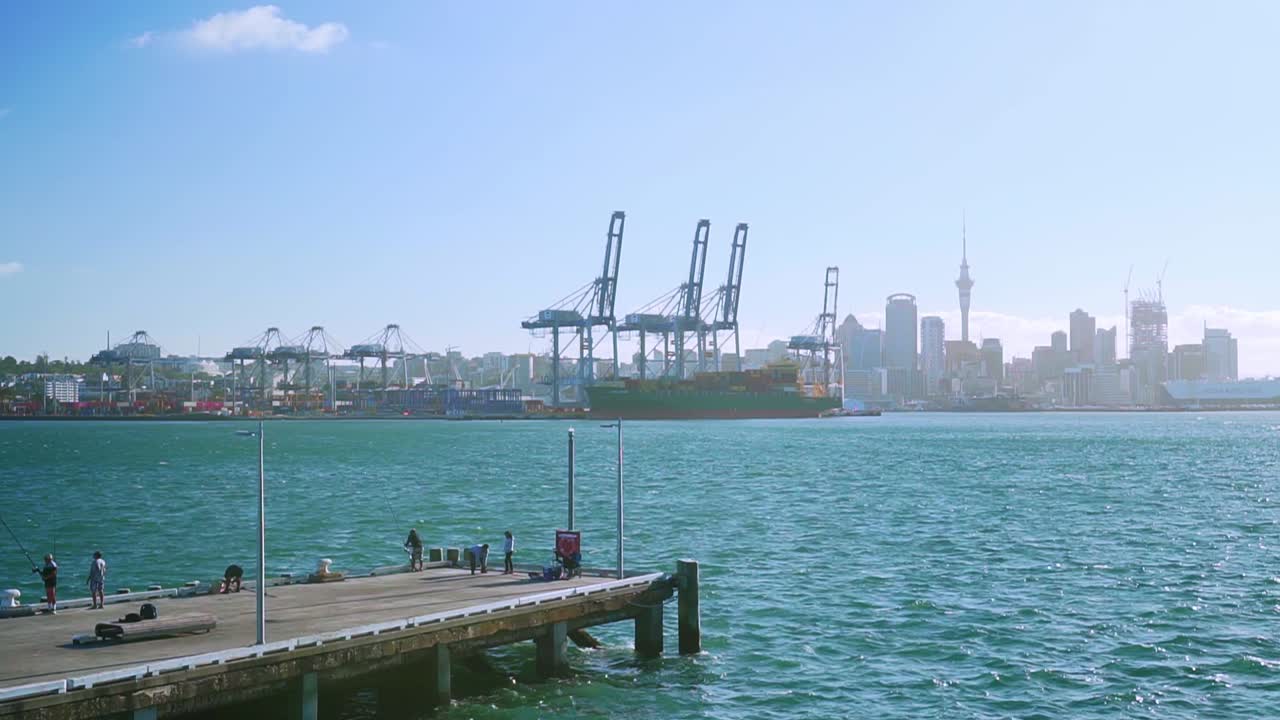 slowmo - 사람들이 낚시를 하는 데번포트 부두, 오클랜드 항구, 스카이라인을 배경으로 패닝 샷, 뉴질랜드