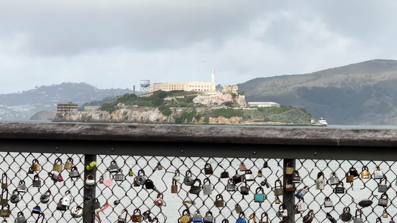 Alcatraz prison in the background on a cloudy day and a railing with love locks in the foreground STATIC SHOT