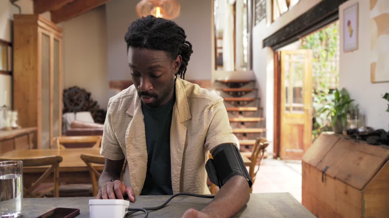 African American man placing cuff, operating monitor, checking blood pressure at dining table