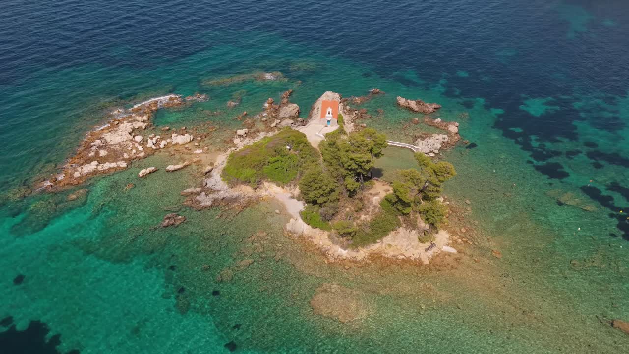 Smooth orbiting shot around a small island featuring a charming chapel, surrounded by crystal-clear waters and natural beauty