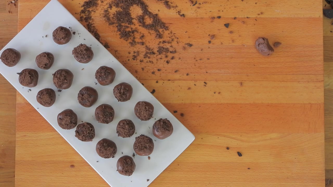 Pessoa enrolando trufas de chocolate caseiras em uma mesa de madeira