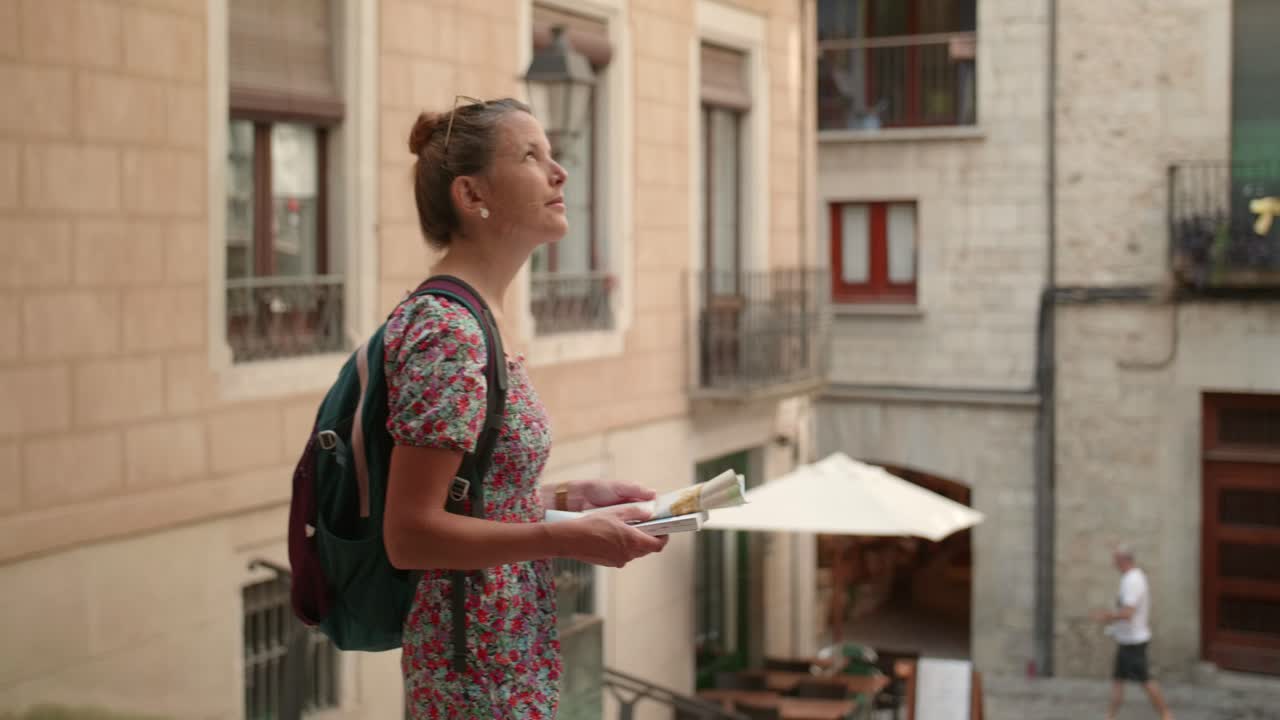 Donna che tiene in mano una guida turistica mentre si guarda intorno tra gli edifici