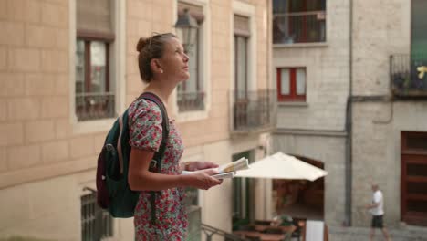 woman holding a tourist handbook while looking around the buildings