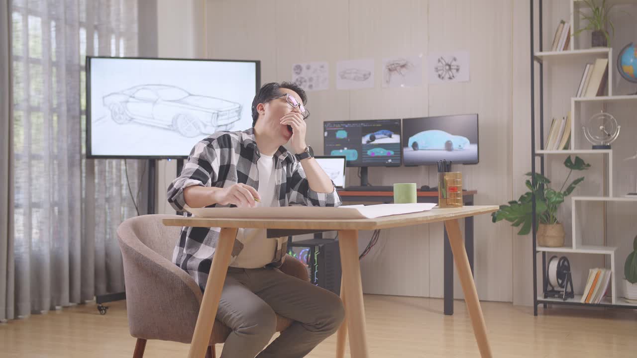 hombre asiático bostezando y durmiendo mientras trabaja en un boceto de diseño de coche en la mesa en el estudio con tv y computadoras muestran modelo de coche eléctrico 3d