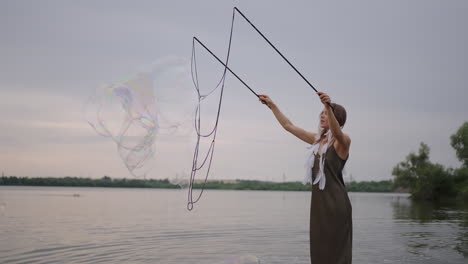 a young girl artist shows magic tricks using huge soap bubbles. create soap bubbles using sticks and rope at sunset to show a theatrical circus show