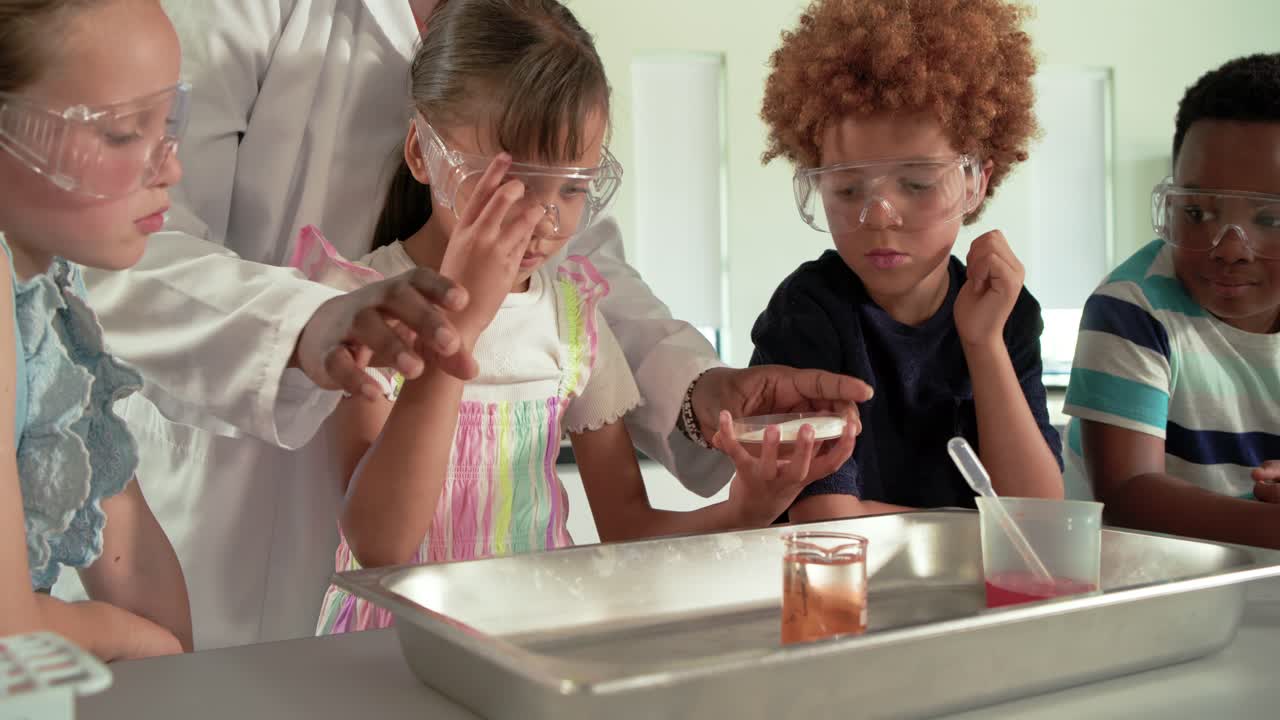 Teacher in lab coat guiding kids in lab, pointing girl using dropper inspecting orange liquid