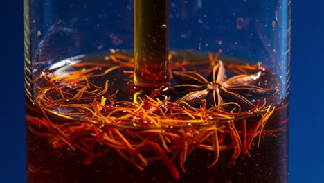 a close-up exploration of aromatic infusion featuring saffron and star anise in a crystal clear vessel against a vivid blue background