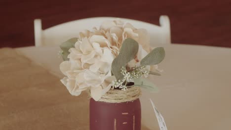 a homemade rustic arrangement of white flowers in a red painted jar in the center of a reception table