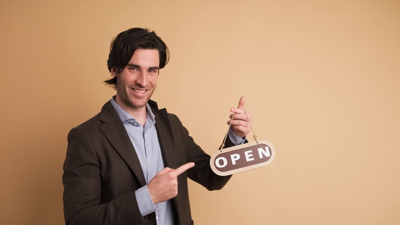 Smiling businessman with open sign inviting in brown studio