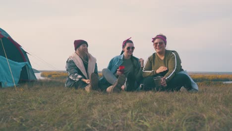 girl friend tourists rest talking on grass by tent at sunset